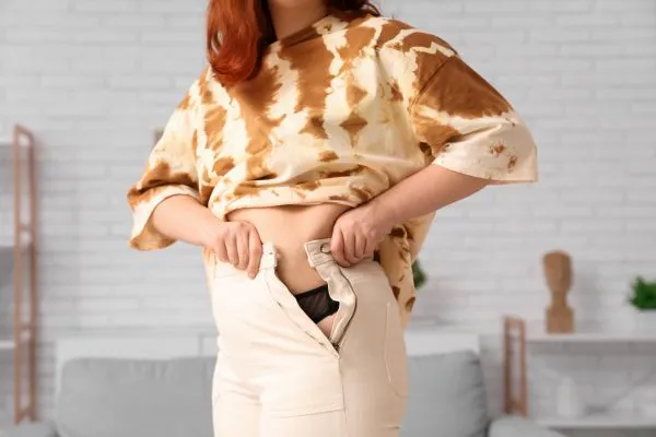 Image of woman trying to do her trousers up after pregnancy weight gain Salisbury